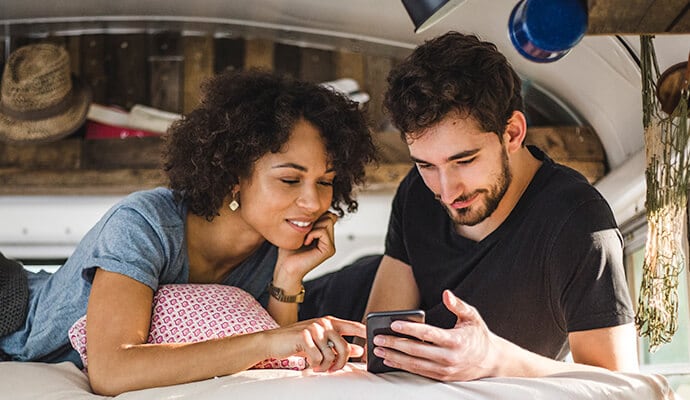 mand, der spiser et måltid og kigger på en mobiltelefon med Norton 360 Standard installeret.